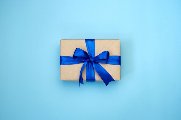 Gift box with blue ribbon bow wrapped in craft paper on blue background.