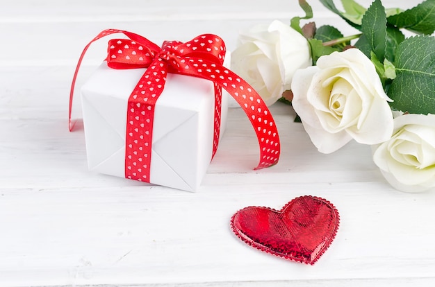 Gift box with bouquet of white rose on white wooden table.