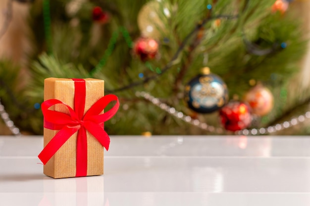 Gift box with bow and blurred Christmas tree with toy balls