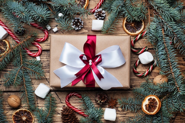 Gift box with bow. Christmas tree and decorations, cane caramel and oranges nuts Wooden background