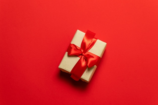 A gift in box with a bow on a red background with hearts. The concept of the day of St. Valentine