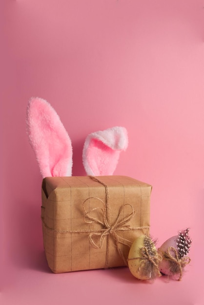 Gift box with cute bunny ears and easter eggs on pink background copy space