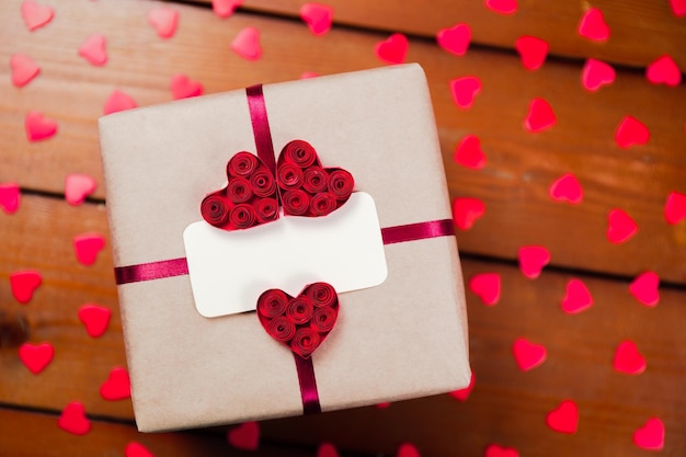 Gift box with empty tag and red ribbon and red hearts Top view