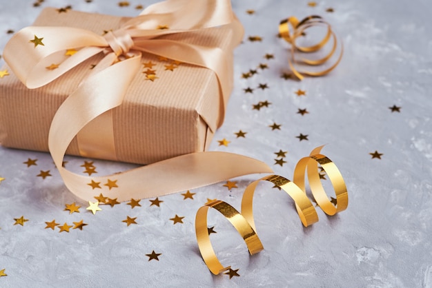 Gift box with golden bow and confetti, close up