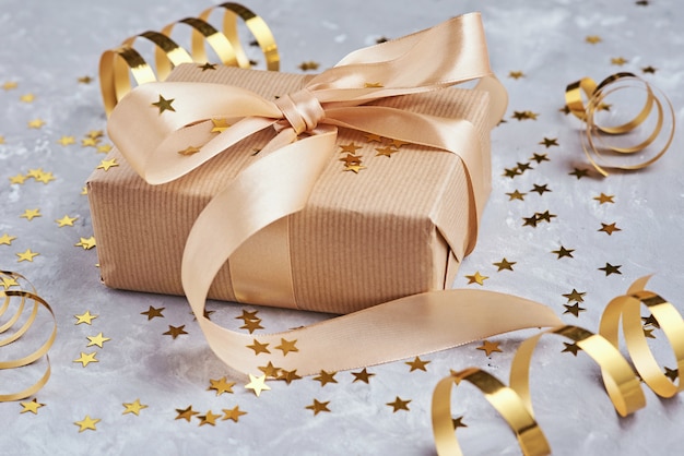 Gift box with golden bow and confetti, close up