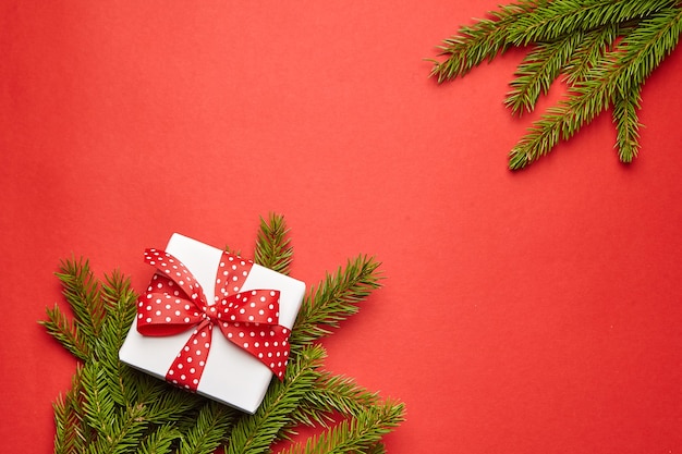 Gift box with green Christmas tree branch on red background top view