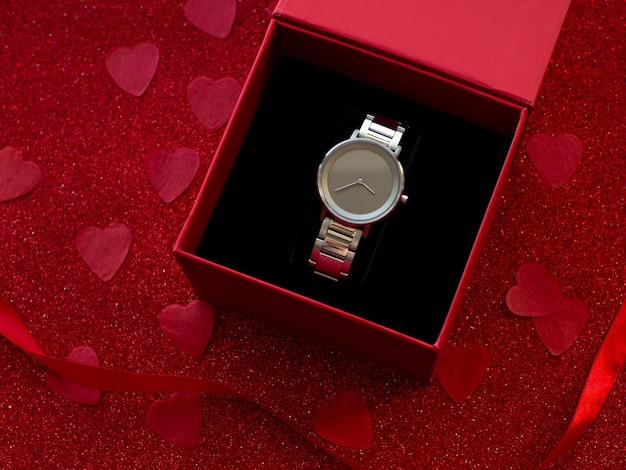 Gift box with silver watch is on red heart paper background