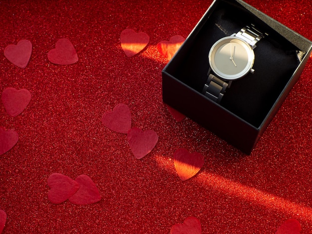 Gift box with silver watch is on red heart paper background