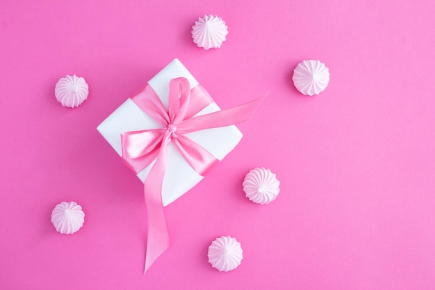 Gift box with tied pink bow and macaroon on the pink background Closeup Top view