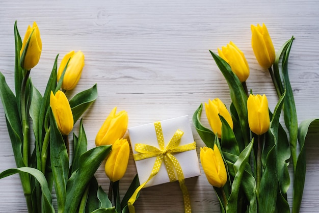 Gift box with tulips on white wooden background Space for message Flowers concept Holiday greeting card for Valentine's Women's Mother's Day Easter Birthday Top view flat lay