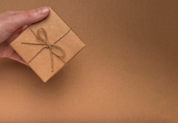 Gift box wrapped in craft paper with jute bow in female hand on eco kraft cardboard