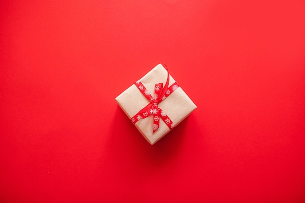 Gift box wrapped in craft paper with red ribbon bow and copyspace on red background