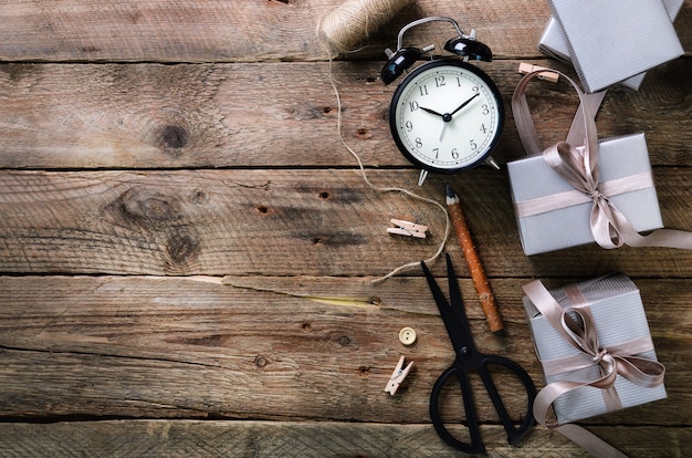 Gift boxes, black alarm clock, pen, scissors on wooden. Preparing for birthday, christmas, new year.