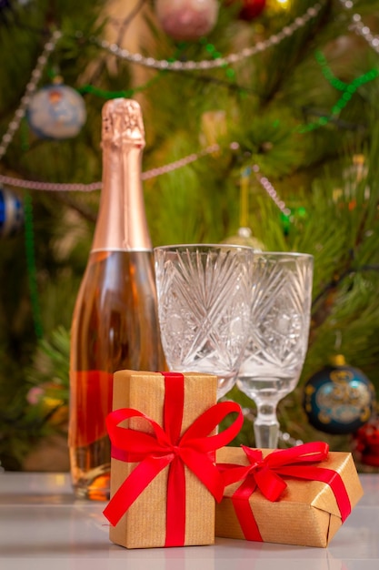 Gift boxes and blurred crystal glasses bottle of champagne and Christmas tree with toy balls