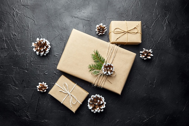 Gift boxes and green Christmas tree branch with cone on dark background top view