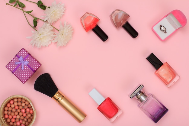 Gift boxes, powder, nail polish, bottle of perfume, brush and flowers on a pink background. Women cosmetics and accessories. Top view.