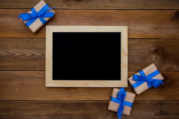 Gift boxes with blue ribbon and empty chalkboard on wooden table. Top view.