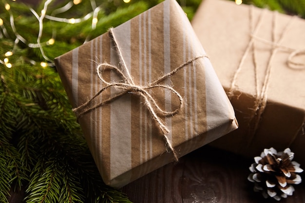 Gift boxes with Christmas light and tree branch with cone on brown wooden background