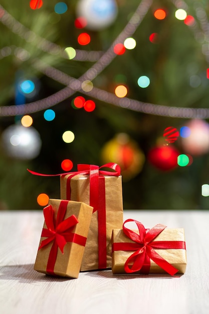 Gift boxes with red bows and blurred Christmas tree with twinkling party lights and toy balls