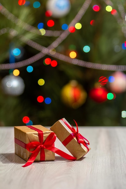 Gift boxes with red bows and blurred Christmas tree with twinkling party lights and toy balls