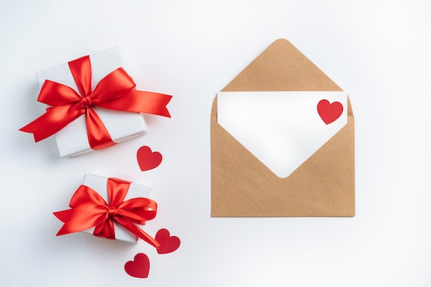 Gift boxes with red ribbon and brown envelope with blank card on white