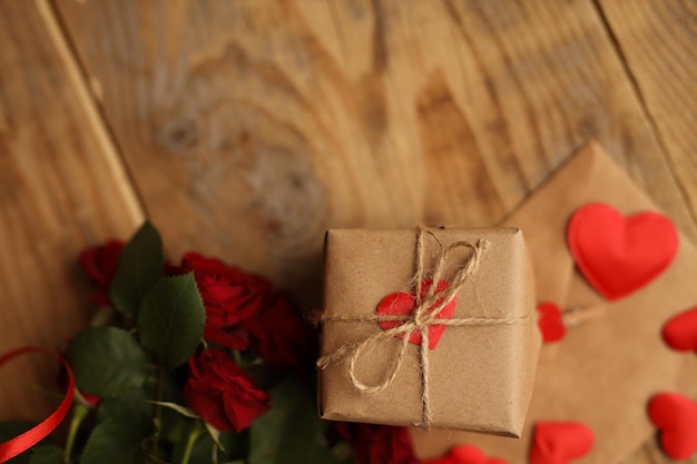 A gift in craft paper on a wooden background around red roses and hearts The 14th of February