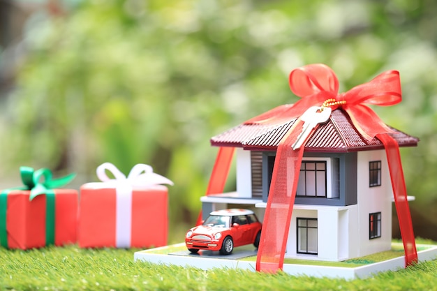 Gift new home and Real estate concept,Model house with Red ribbon and the car on natural green background