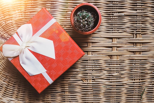 Gift red box with white ribbonon woven bamboo wood background cozy and warm home welcome concept ide and small lovely green cactus