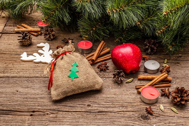 Gift in sack, New Year tree, apple, candles, spices, deer, cones. Nature decorations, vintage wooden boards