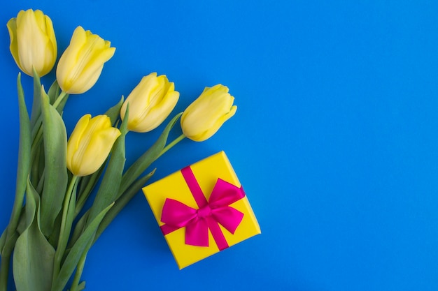 Gift with pink bow and yellow tulips on blue