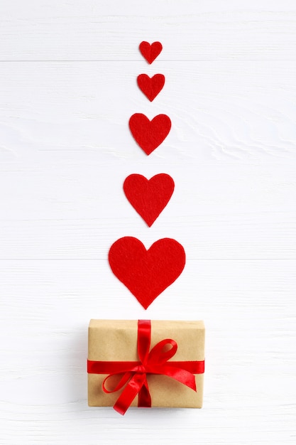 Gift with red ribbon and hearts on white wooden background