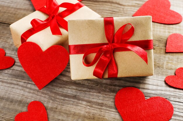 Gift with red ribbon and hearts on wooden background