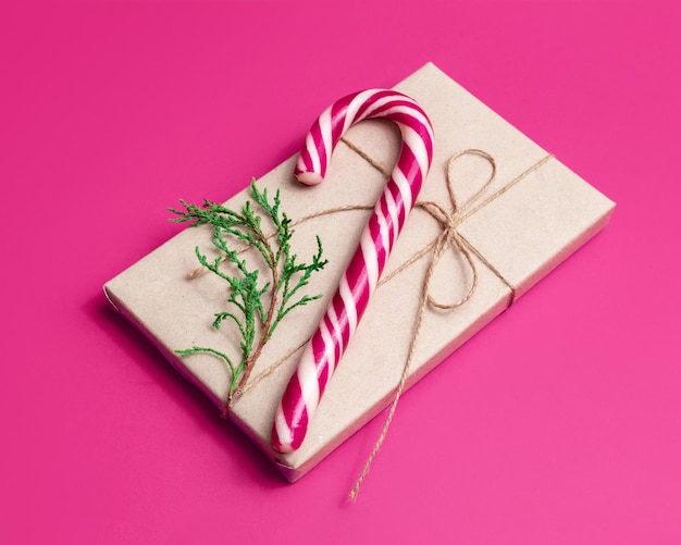 Gift wrapped in craft paper and candy cane on pink background New Year or Christmas concept