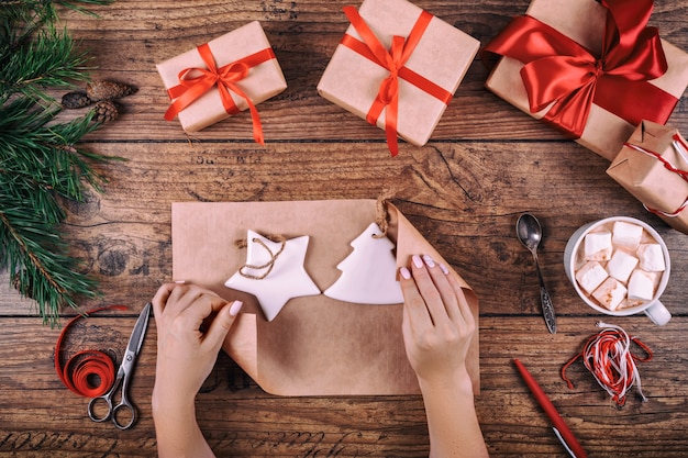 Gift wrapping background. Female hands packaging handmade Christmas decorations to christmas present in kraft paper