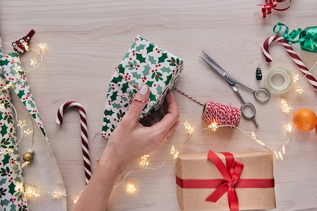 Giftboxes, presents wrapping with paper and ribbon, lights, candy canes on wooden background. Holdiay DIY handmade home decoration