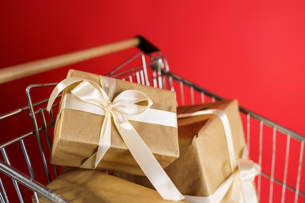 Gifts in craft paper with white tape in a supermarket trolley on a red background