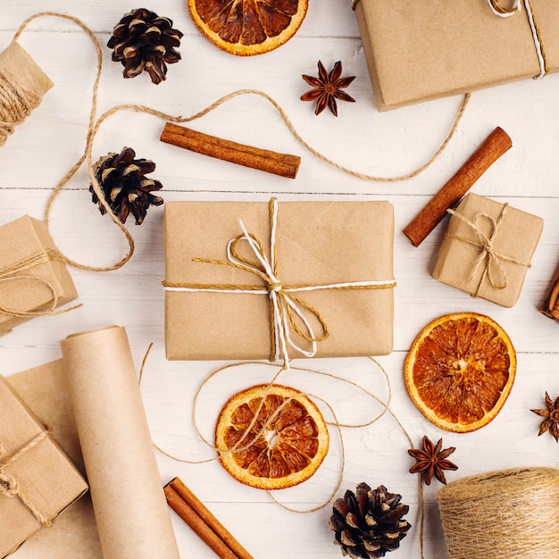 Gifts from craft paper, dried orange, cinnamon, pine cones, anise on a white table The original decor for Christmas.