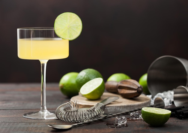 Gimlet Kamikaze cocktail in modern glass with lime slice wooden background with fresh limes and strainer with shaker.