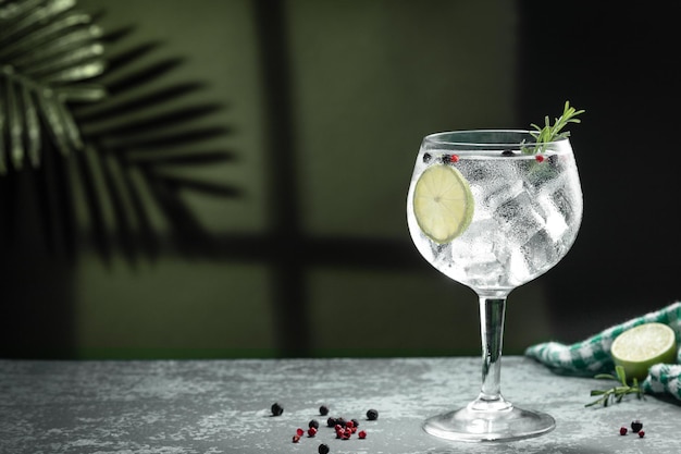 Gin tonic cocktail and shadows next to the window on dark concrete background