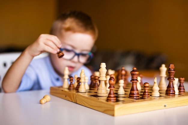 Ginger boy with down syndrome with big glasses playing chess at home