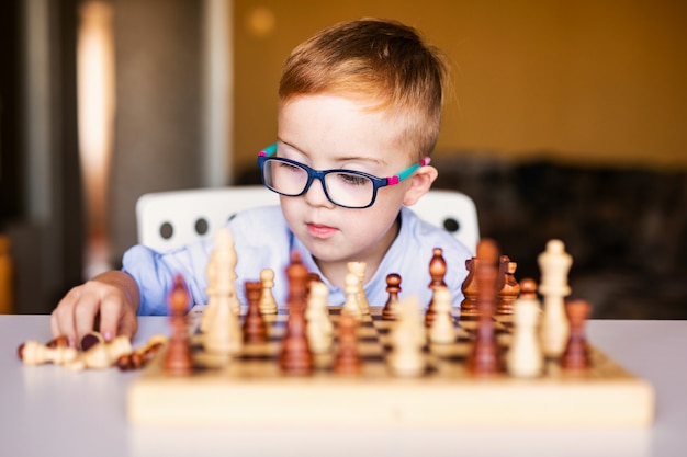 Ginger boy with down syndrome with big glasses playing chess at home