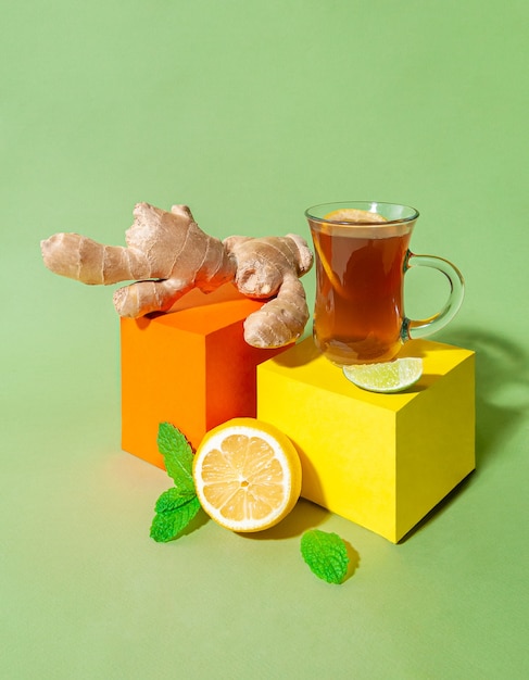 Ginger drink with lemon in a transparent glass mug. Next to it is ginger root, cardomom, mint and lime.