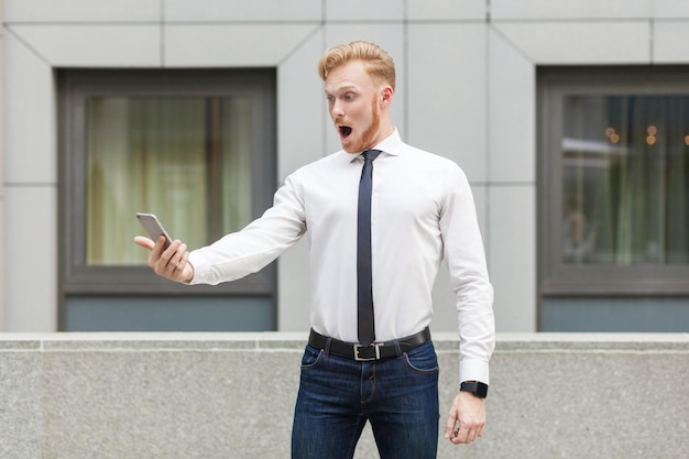 Ginger young adult business person looking at screen smart phone with shocked face