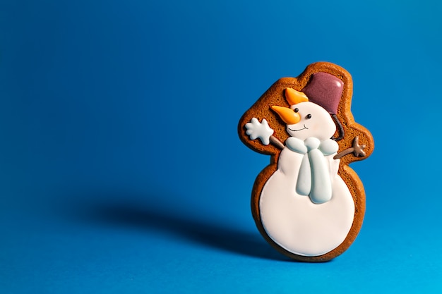 Gingerbread cookie of cute snowman on blue . Traditional Christmas food. Christmas and New Year holiday .