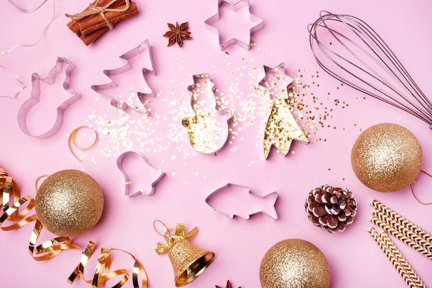 Gingerbread cookie cutters and gold Christmas decor on a pink background. Flat lay style