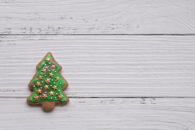 Gingerbread cookie of green Christmas tree on white wood background