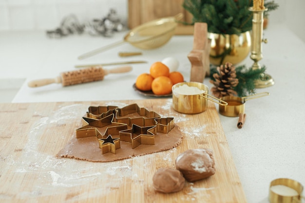 Gingerbread dough with festive golden metal cutters on wooden board with flour cooking spices festive decorations in modern white kitchen Making christmas gingerbread cookies