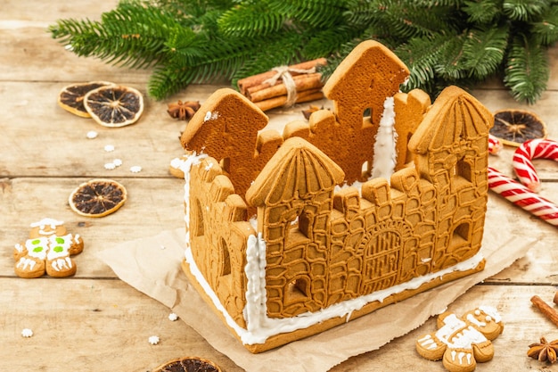 Gingerbread House decorated by sweet icing. Handmade process, festive New Year decor. Traditional spices, wooden background