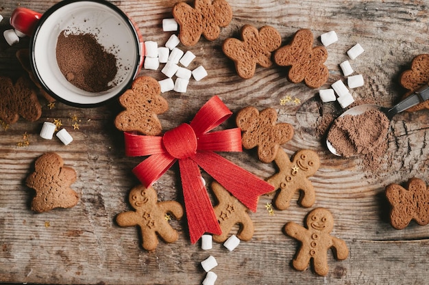 Gingerbread man cocoa and cookies with a big red bow on a wooden background top view Various christmas sweets with a cup of cocoa on the table