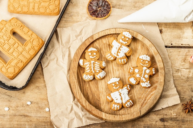 Gingerbread men decorate sweet icing. Traditional festive decor, cooking process. Old wooden background, homemade concept, top view